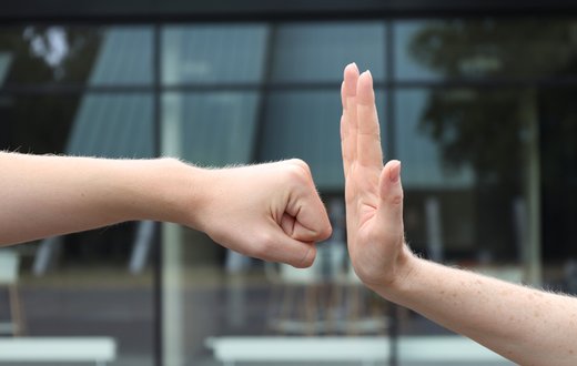 Zwei Hände in Konfliktpose vor einem modernen Gebäude.