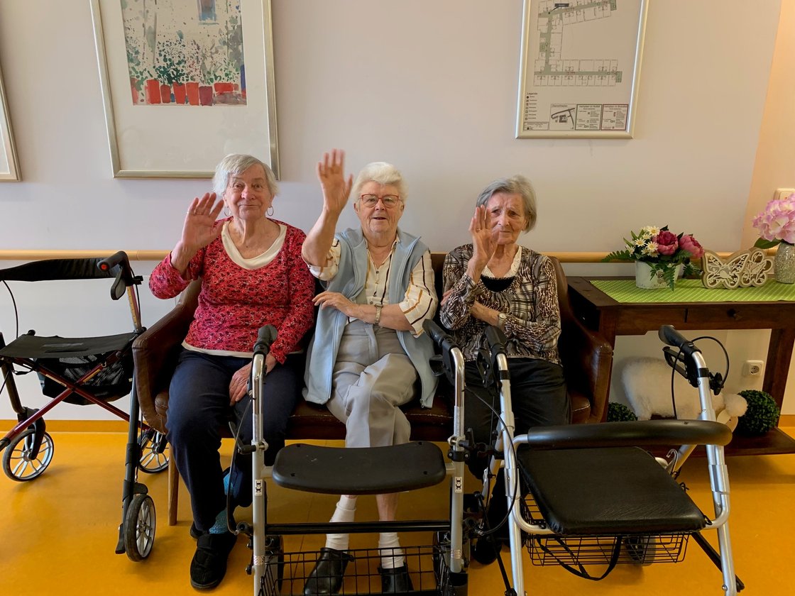 Drei Seniorinnen im Seniorenzentrum Eckental winken, umgeben von Rollatoren.