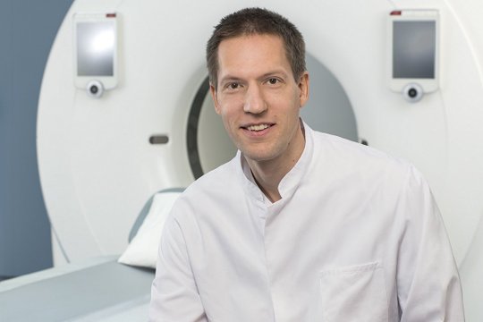 Arzt in weißem Kittel vor CT-Scanner im Krankenhaus.