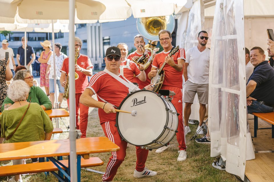 Band in roten Outfits spielt auf Sommerfest, Menschen sitzen an Tischen.