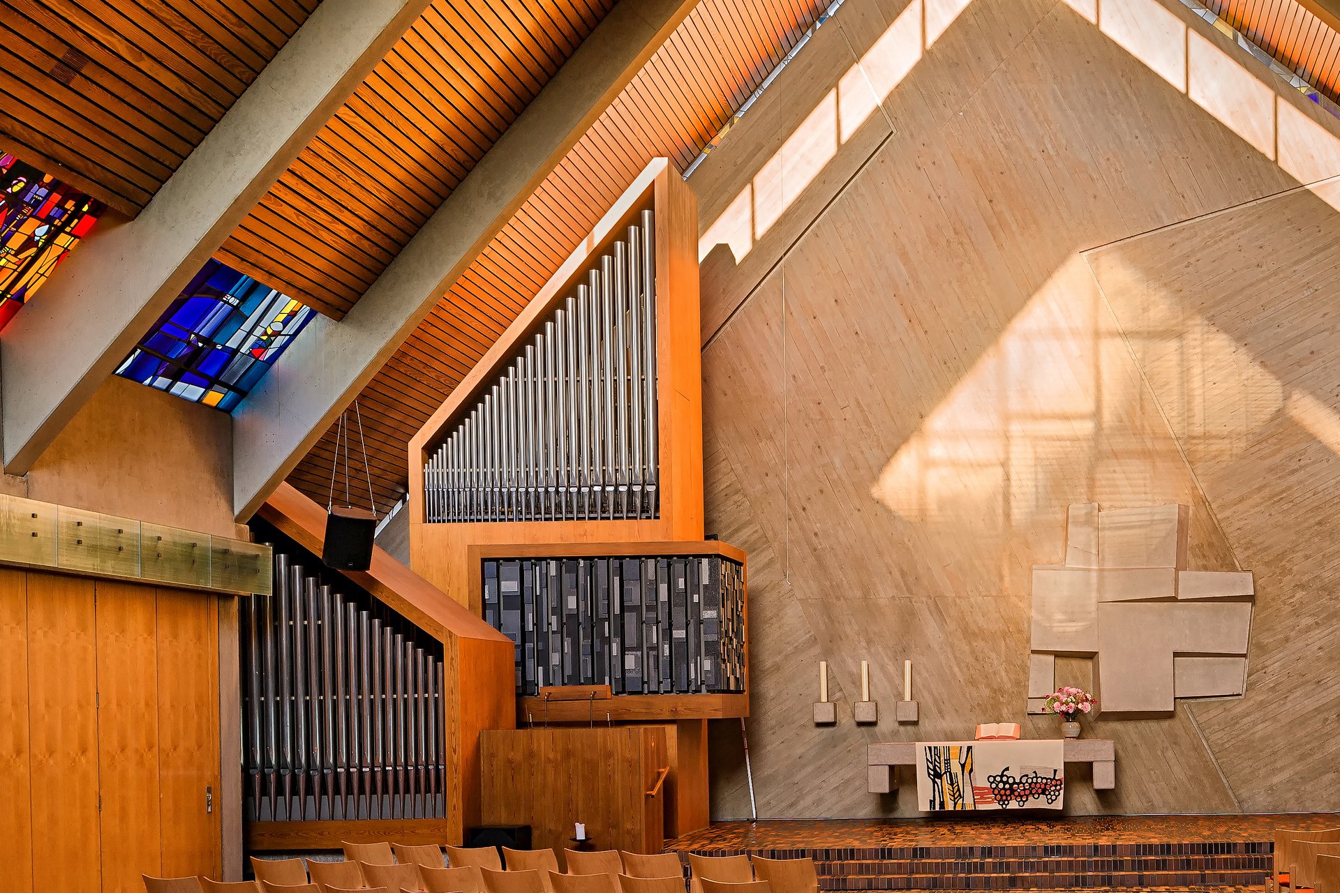 Innenraum einer modernen Kirche mit Orgel, buntem Glasfenster und Altar.