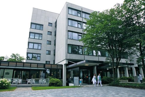 Krankenhausgebäude mit Bäumen und Ärzten im Vordergrund.