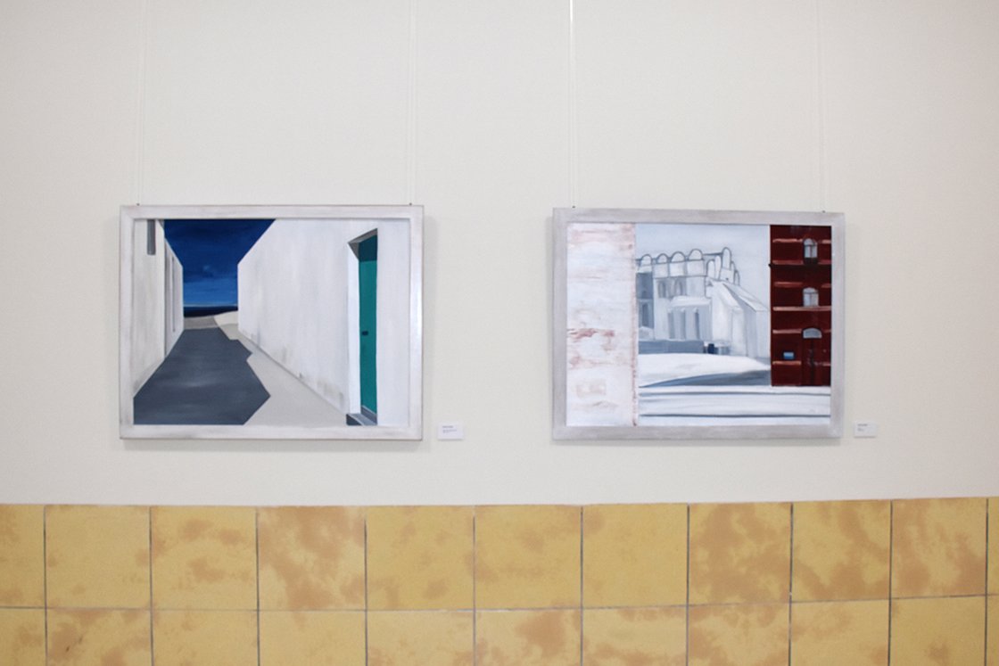 Zwei gerahmte Gemälde an einer Galerie-Wand hängend, moderne Architektur darstellend.