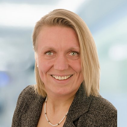 Porträt einer lächelnden Frau mit blondem Haar und Perlenkette.