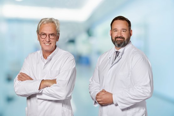 Zwei Ärzte in weißen Kitteln stehen in einem modernen Krankenhausflur.