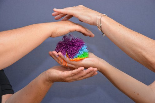 Drei Hände halten bunten, stacheligen Ball symbolisch behutsam im Kreis.