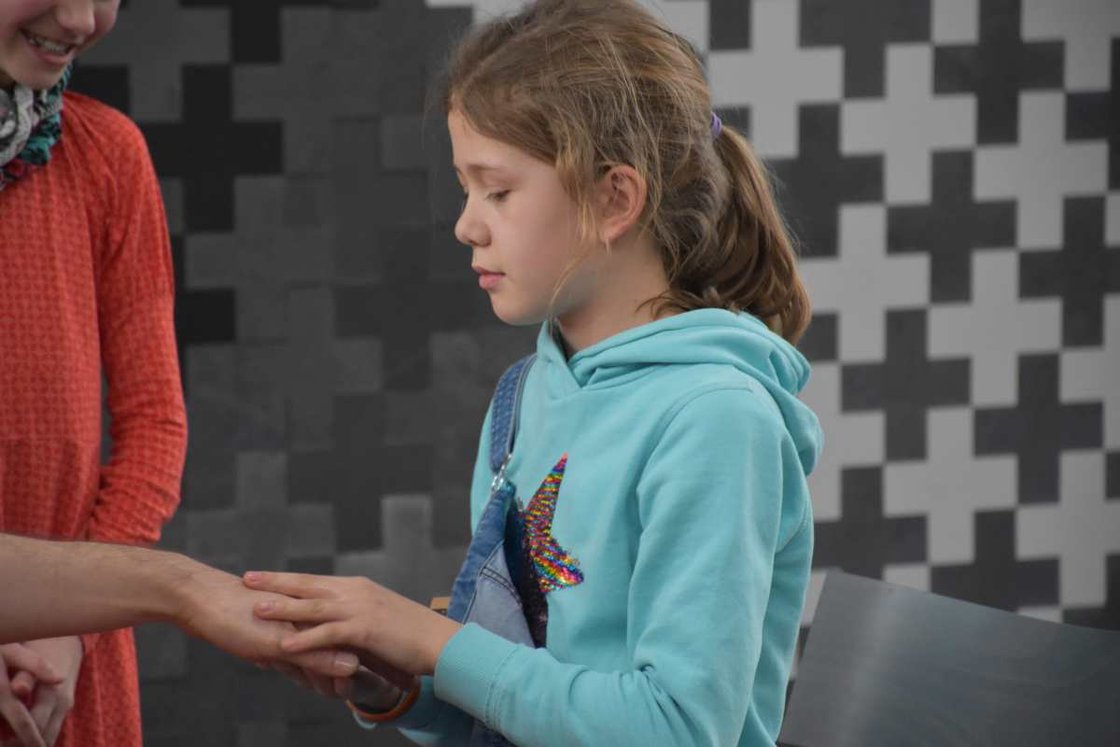 Mädchen in blauem Hoodie hält sanft eine Hand, konzentriert.