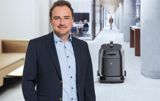 Mann in Büroflur neben einem Reinigungsroboter, symbolisiert innovative Arbeitsumgebung.