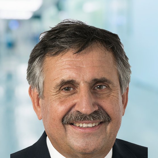 Porträt eines lächelnden Mannes vor unscharfem, hellen Hintergrund.