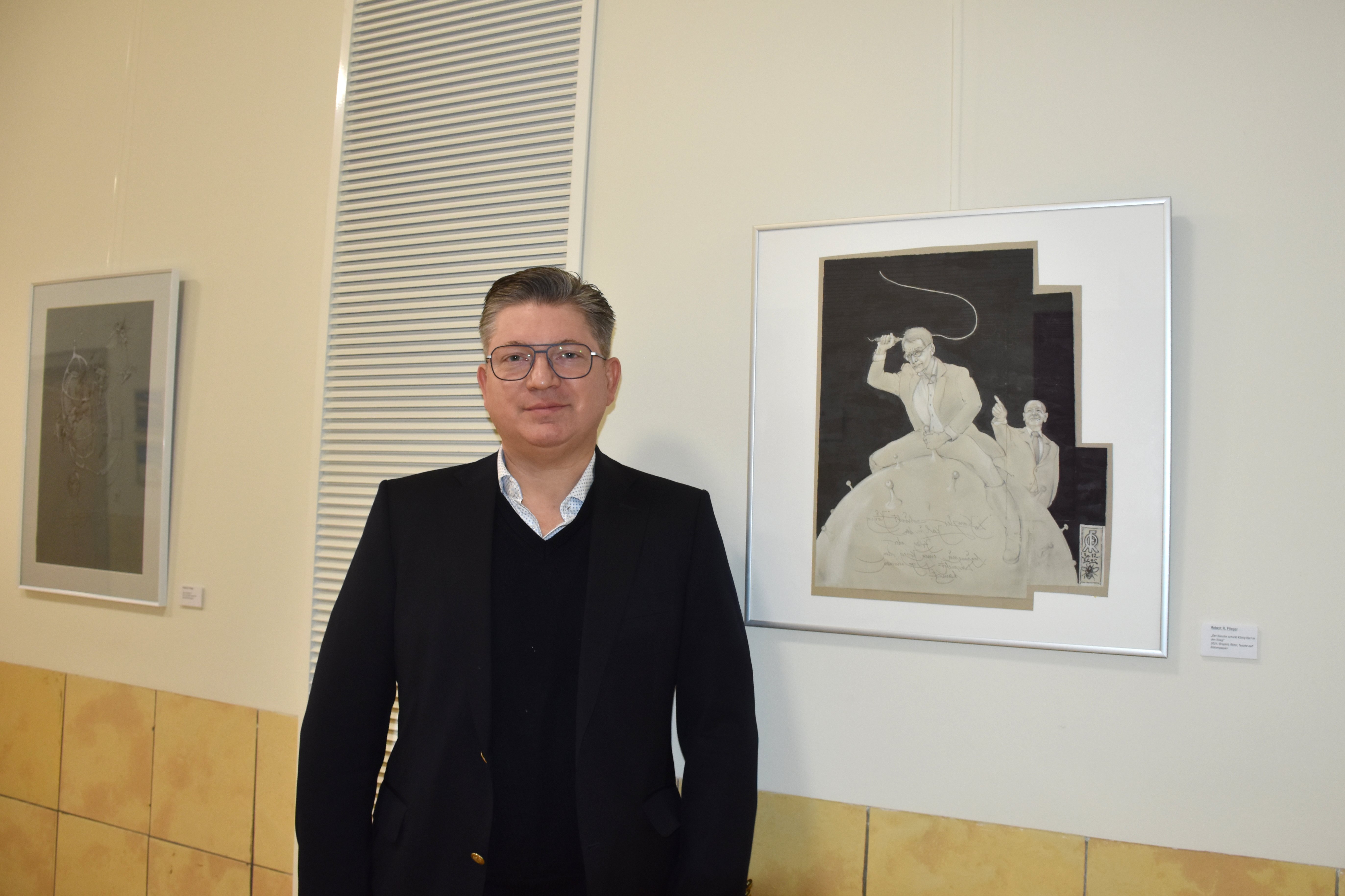 Mann steht vor Kunstwerken in einer Galerieausstellung.