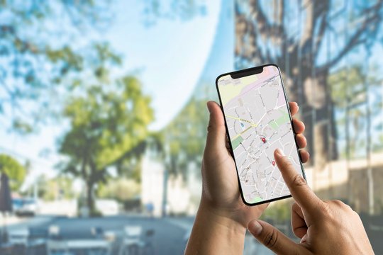 Person hält Smartphone mit Karten-App vor verschwommenem Hintergrund.