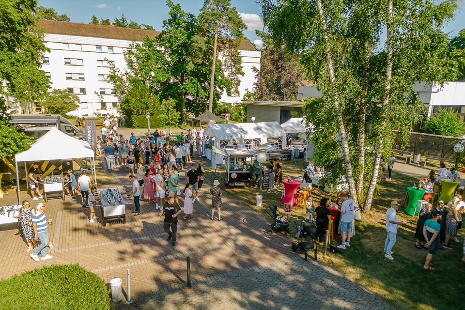 Luftaufnahme eines Sommerfestes im Freien mit Ständen und Besuchern.