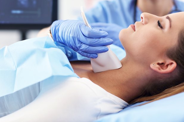 Ärztin führt Ultraschalluntersuchung am Hals einer Patientin durch.