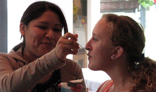 Zwei Frauen, eine füttert die andere mit einem Löffel.