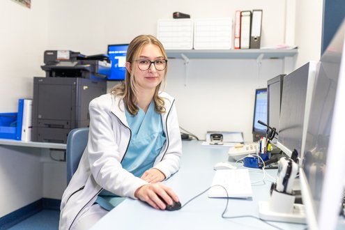 Medizinische Fachkraft im Büro, arbeitet am Computer, trägt Brille und Kittel.