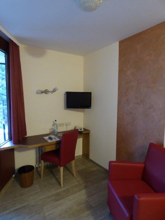 Krankenhaus-Einzelzimmer mit Schreibtisch, Stuhl und Fernseher.