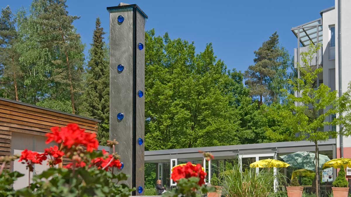 Garten im Seniorenzentrum Nürnberg mit Skulptur und blühenden roten Blumen.