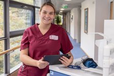 Pflegemitarbeiterin in roter Uniform mit Tablet im Krankenhausflur.