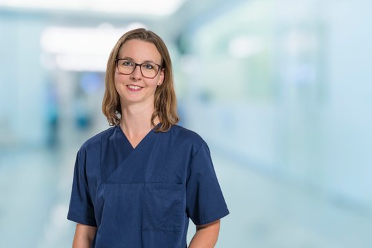 Ärztin in blauer Arbeitskleidung lächelt in einem Krankenhausflur.