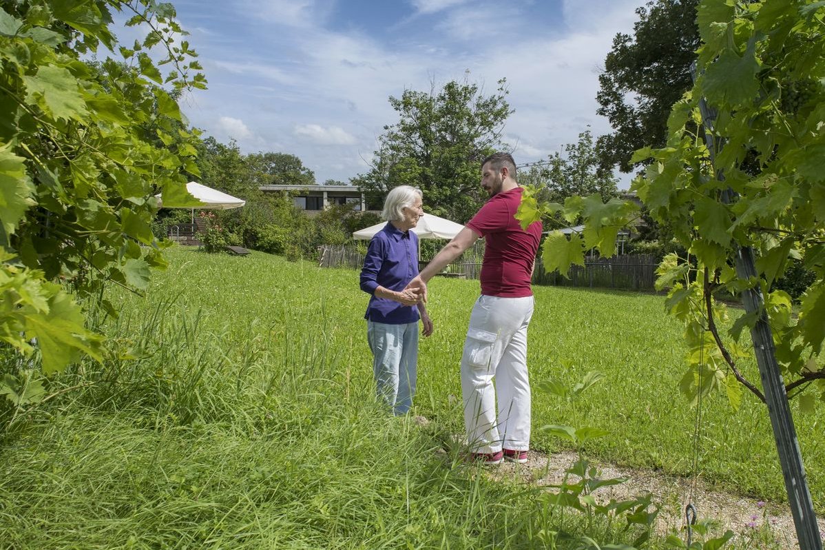 Pflegekraft unterstützt Seniorin bei Spaziergang im Garten des Seniorenzentrums Stuttgart.