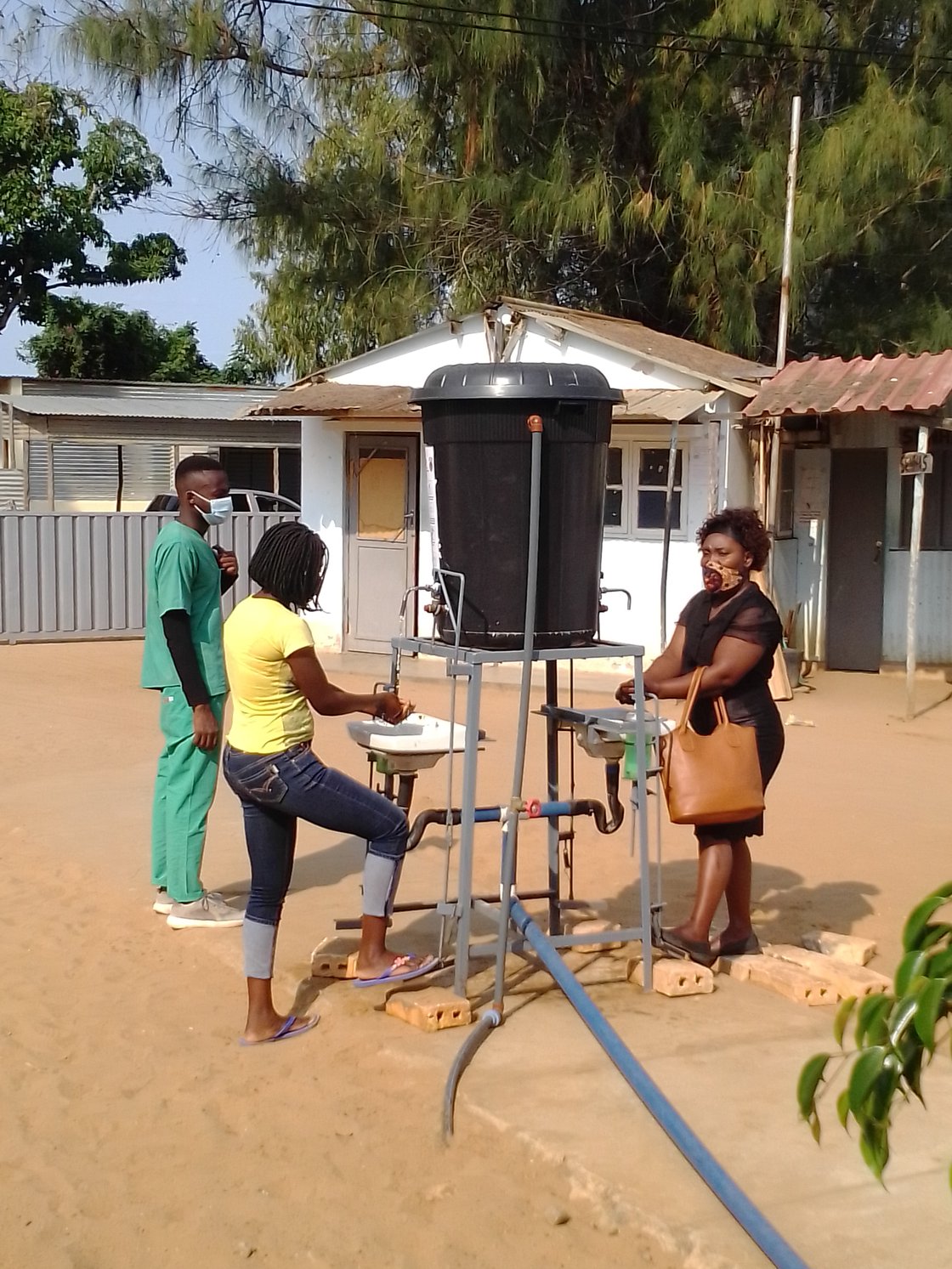 Drei Personen waschen Hände an improvisierter Waschstation im Freien, Mosambik.