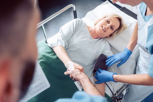Patientin im Krankenhausbett erhält medizinische Versorgung von zwei Pflegekräften.