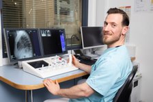 Techniker in Klinik überprüft Röntgenbilder auf Monitoren in Kontrollraum.