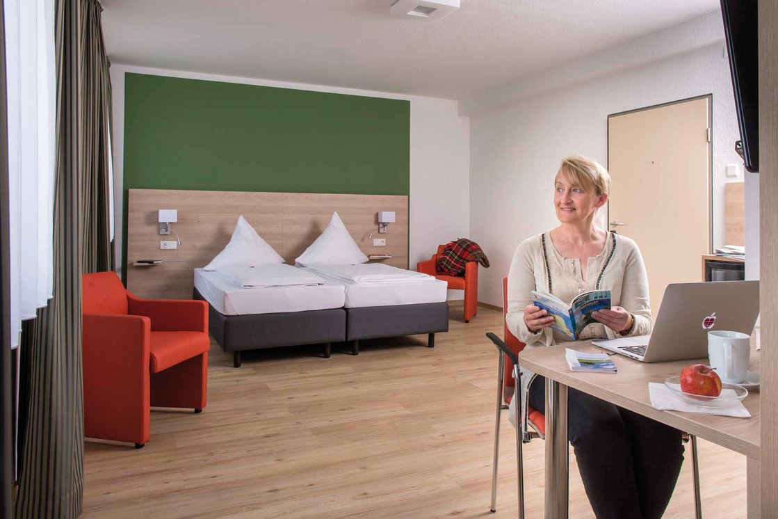 Frau liest in modernem Gästezimmer mit Doppelbett und Schreibtisch.