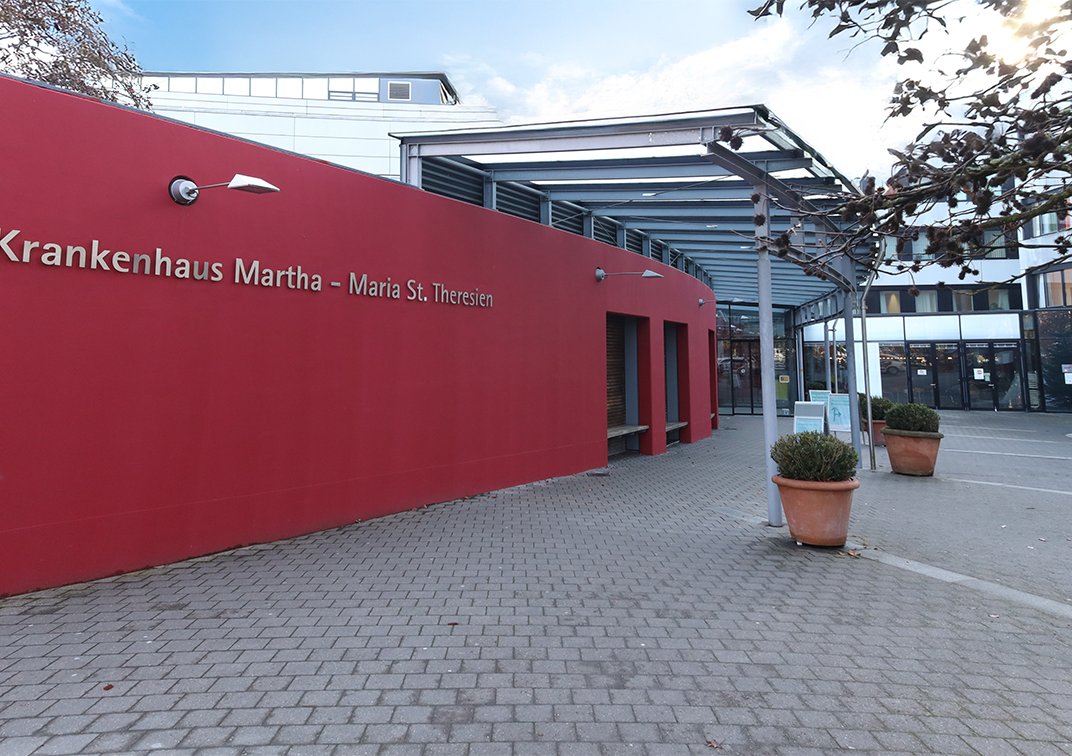 Eingang des Krankenhauses Martha-Maria St. Theresien mit roter Fassade.