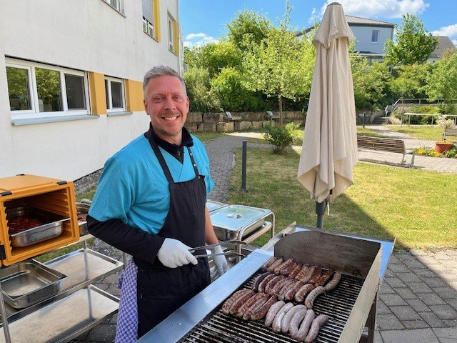 Mitarbeiter grillt Bratwürste im Garten des Seniorenzentrums Eckental.