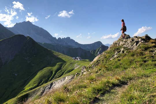 Eine Person steht auf einem Berggipfel im Bergpanorama.