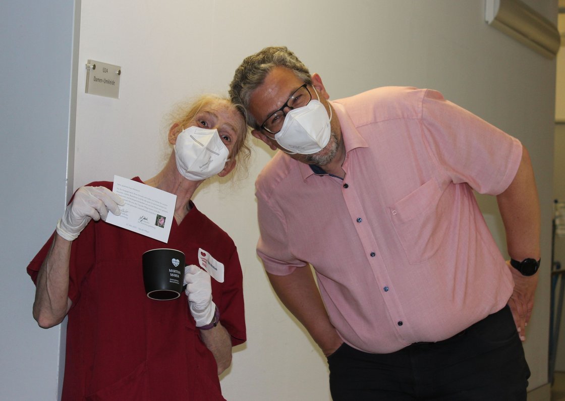 Zwei Personen mit Masken halten Dankeskarte und Tasse vor Umkleideraum.