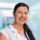 Lächelnde Frau in weißer Bluse vor unscharfem, hellem Hintergrund.