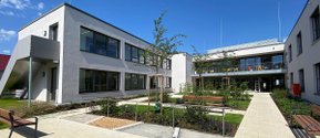 Moderne Martha-Maria-Einrichtung mit Garten und Sitzbänken unter blauem Himmel.