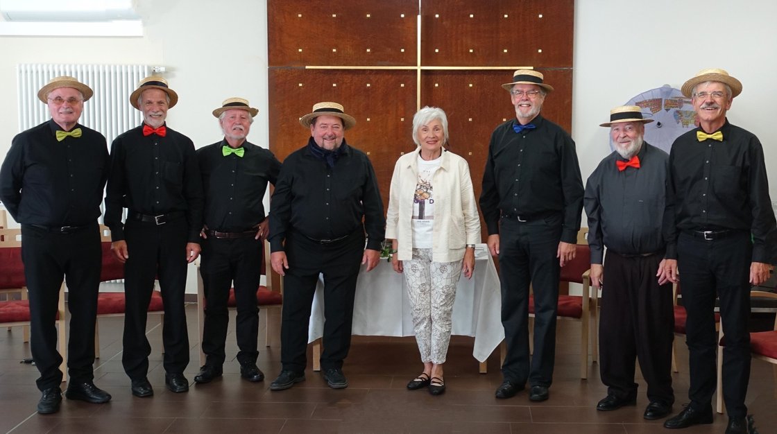 Gruppe von älteren Menschen mit Strohhüten und Fliegen im Seniorenzentrum.