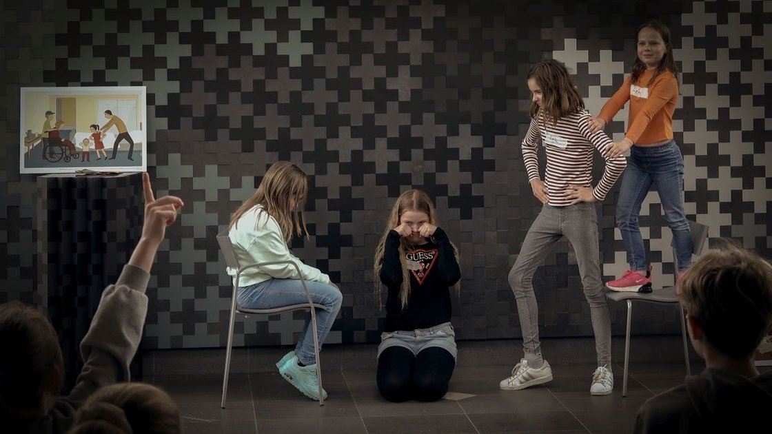 Kinder stellen eine Szene im Krankenhaus dar, Publikum schaut zu.