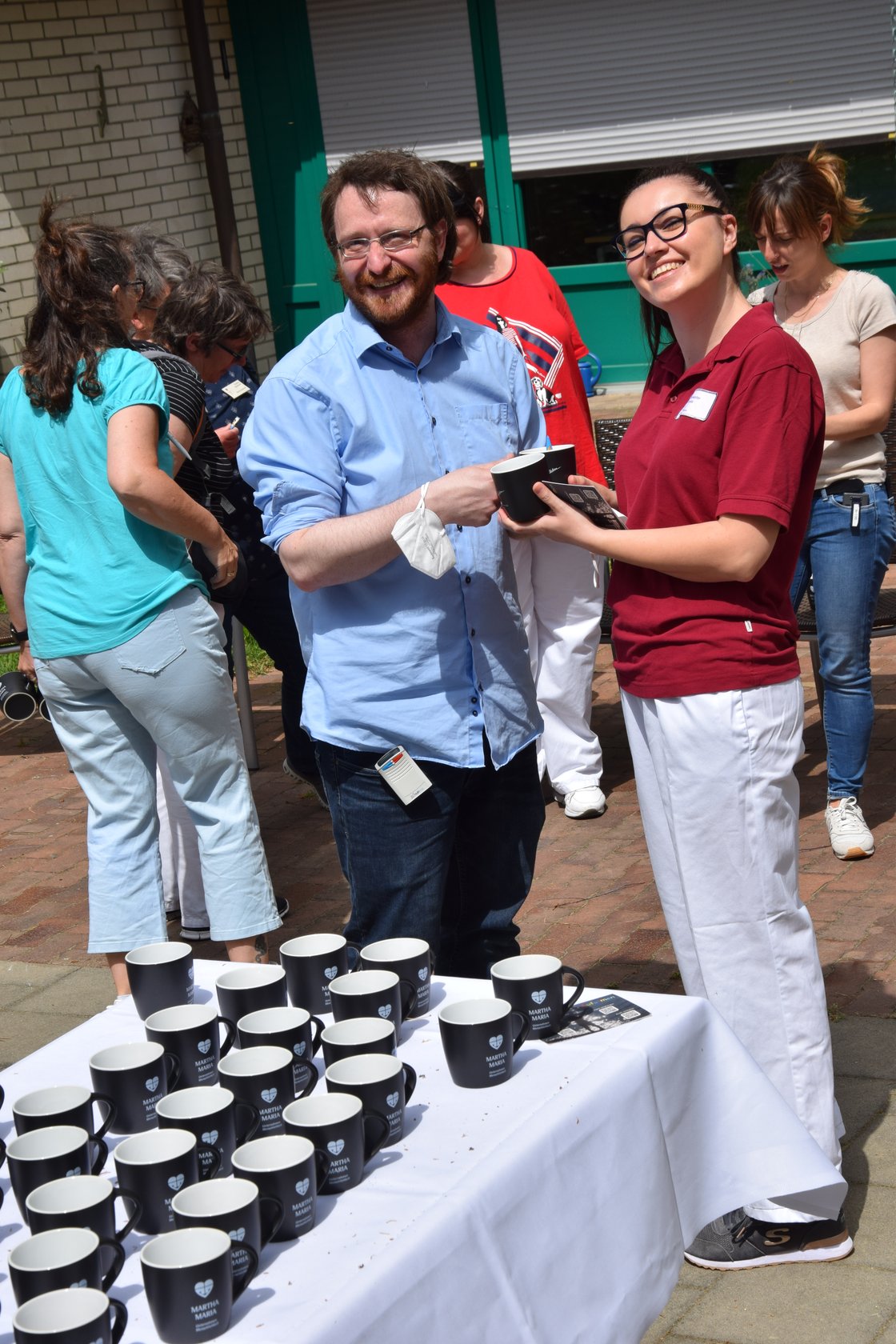 Lächelnde Menschen teilen Tassen bei einer Outdoor-Veranstaltung.