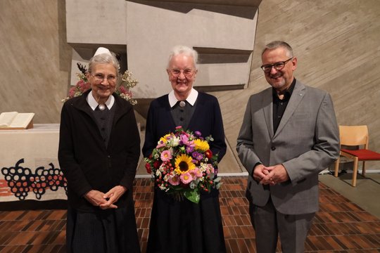 Zwei Diakonissen und ein Mann mit Blumenstrauß in einer Kirche.