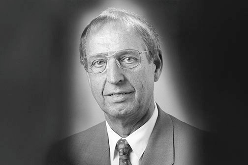 Schwarzweiß-Porträt eines älteren Mannes mit Brille und Anzug.