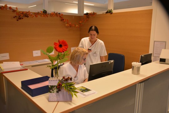Zwei Pflegekräfte an einem Empfangstresen, dekoriert mit Herbstblättern und Blumen.