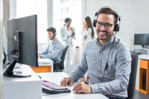 Lächelnder Mann mit Headset arbeitet am Computer in einem modernen Büro.