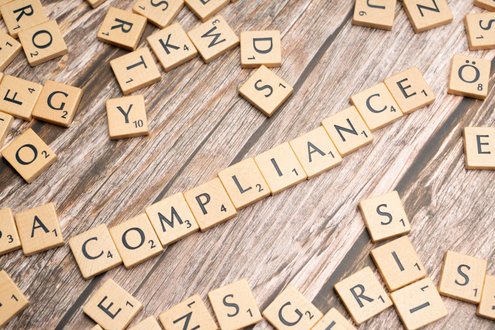 Scrabble-Buchstaben bilden das Wort 'COMPLIANCE' auf Holztisch.