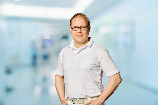 Mann in weißem Hemd steht in hellem Krankenhausflur.