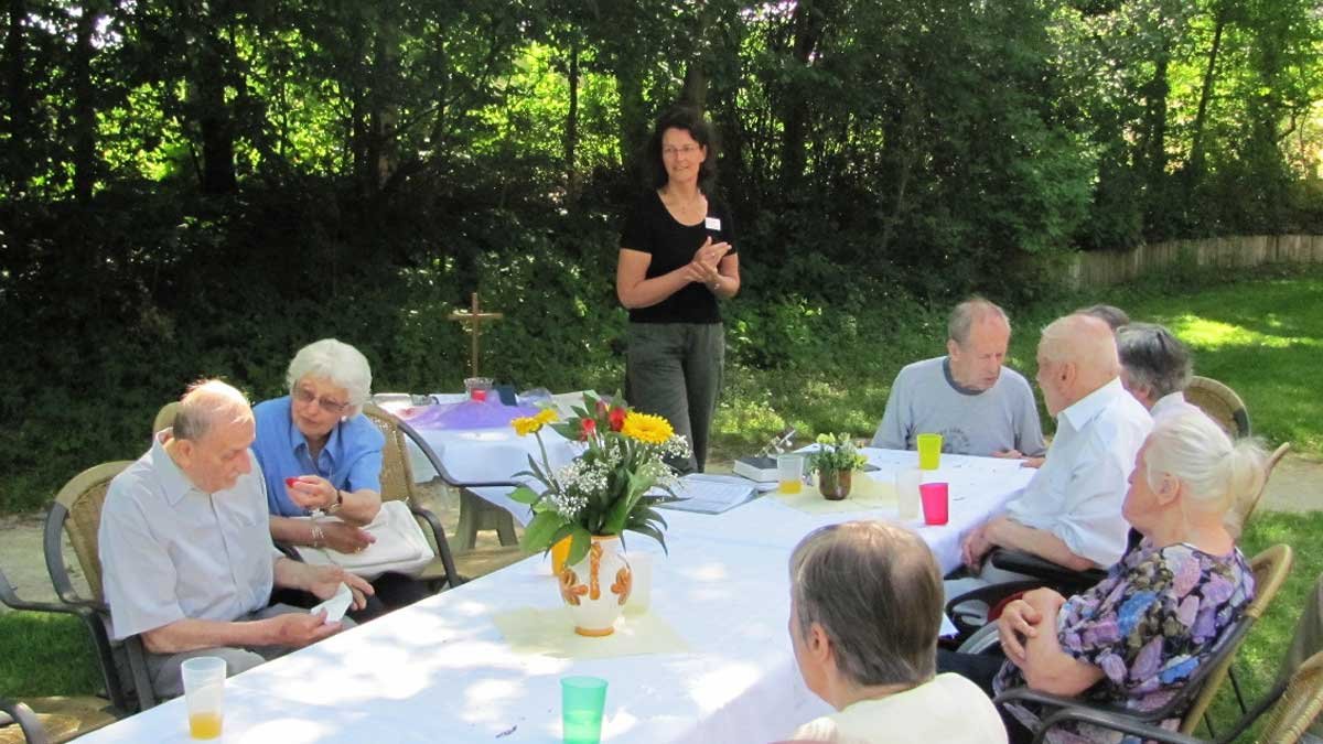 Senioren sitzen draußen am Tisch, betreut von einer Pflegekraft im Seniorenzentrum.