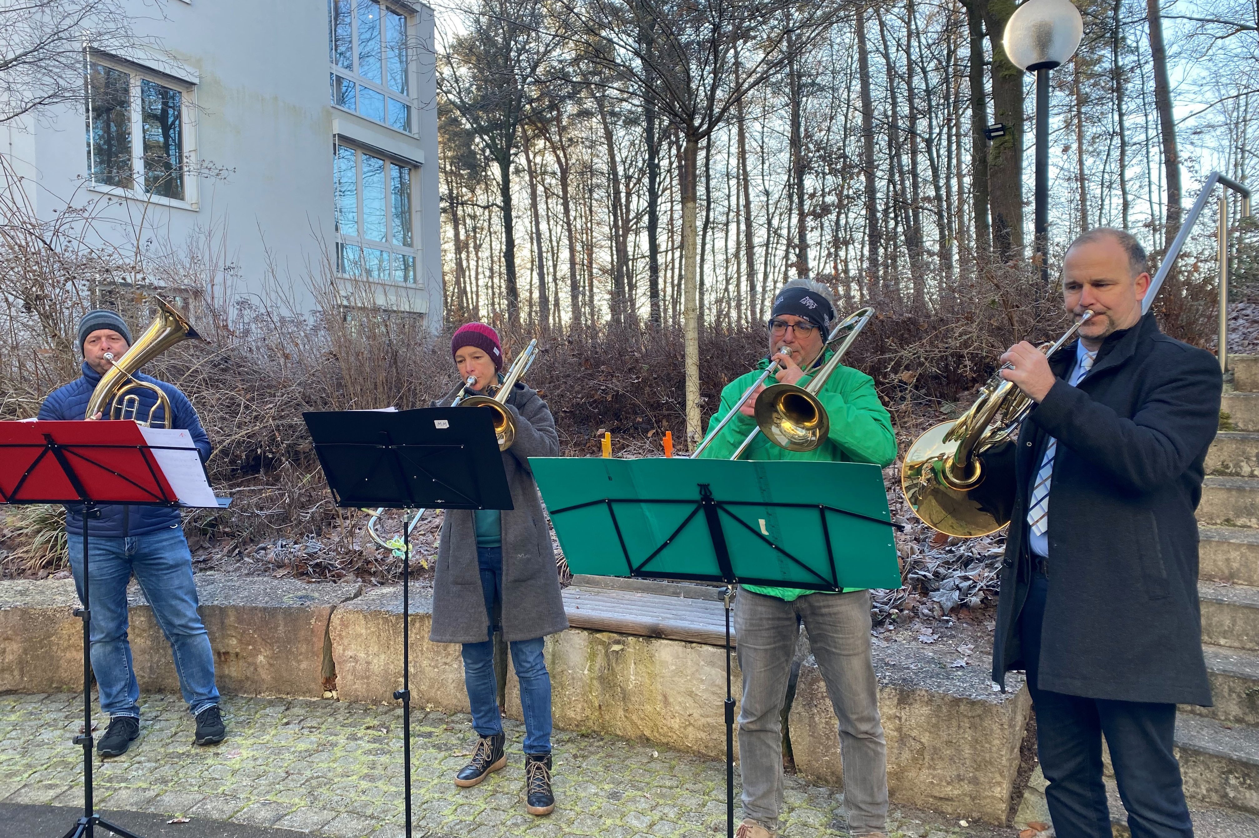 Vier Musiker spielen Blechblasinstrumente vor einem Gebäude im Freien.