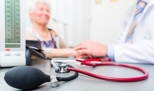 Arzt hält Hände einer älteren Patientin, Stethoskop im Vordergrund.