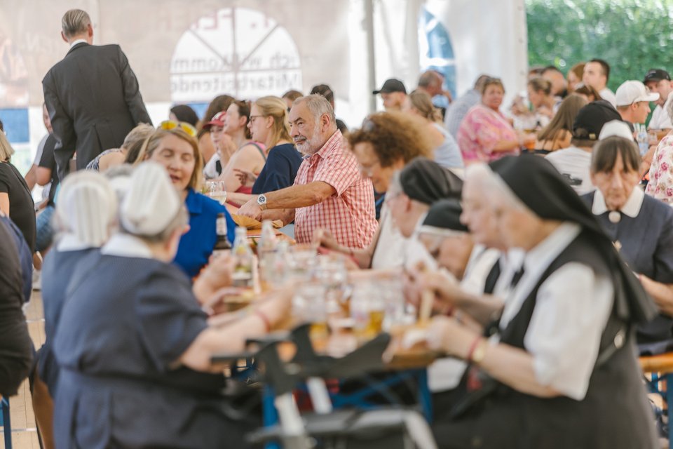 Menschen bei einem Sommerfest im Freien, sitzen an langen Tischen.