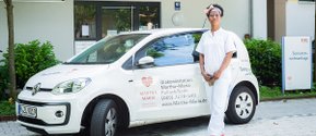 Pflegekraft vor einem Diakonie-Fahrzeug der Martha-Maria Pullach/Solln.