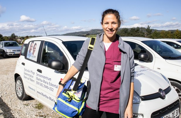 Pflegekraft vor Auto des Seniorenzentrums Eckental, lächelnd, mit Tasche.