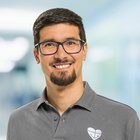 Mann mit Brille und Bart lächelt vor unscharfem Hintergrund im Büro.